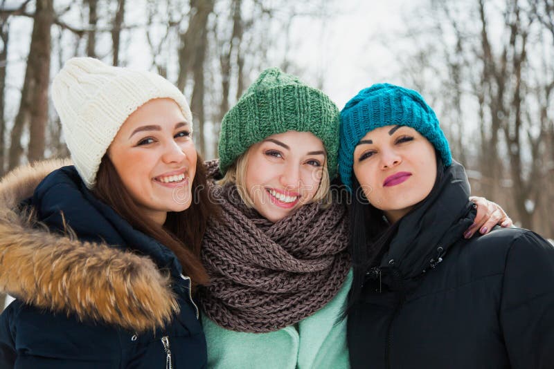 Three women friends outdoors in knitted hats on a snowy cold winter weather.