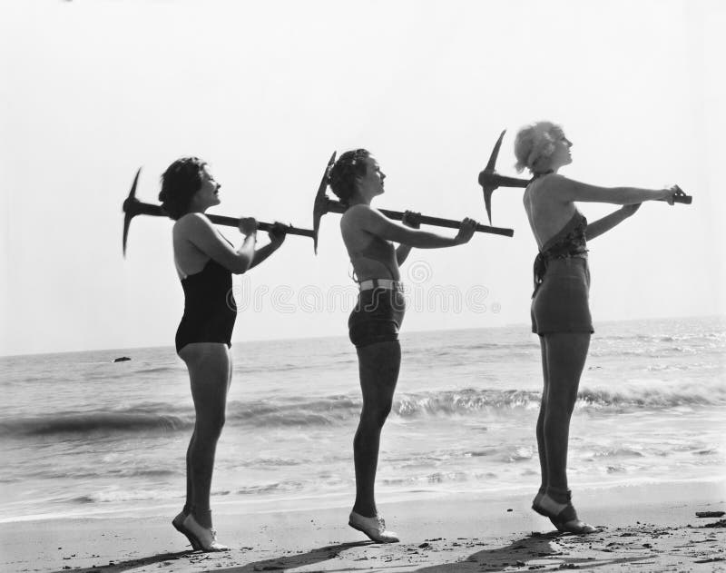Three women posing with a pick ax on the beach