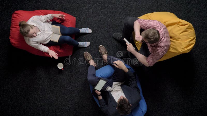 Three workers are sitting on poufs and relaxing, conversation, office concept, communication concept stock video footage