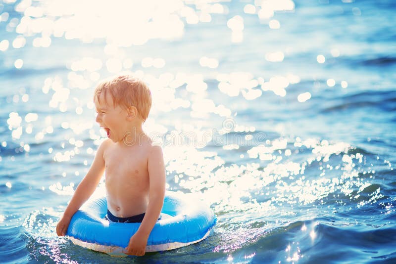 Three years old boy playing at the beach with swimming ring