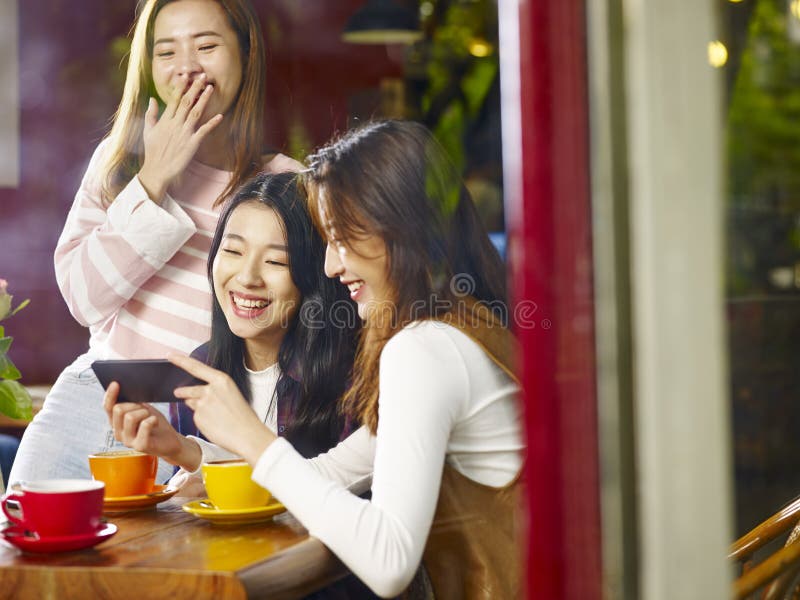 Three young asian women looking at mobile phone and laughing in royalty free stock photography Three young asian women looking at mobile phone and laughing in royalty free stock photography