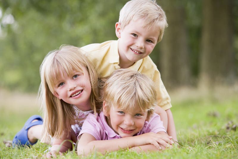 Three young children playing outdoors smiling at camera