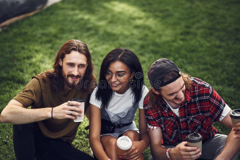 Three young friends enjoying coffee while sitting on the grass together royalty free stock image Three young friends enjoying coffee while sitting on the grass together royalty free stock image