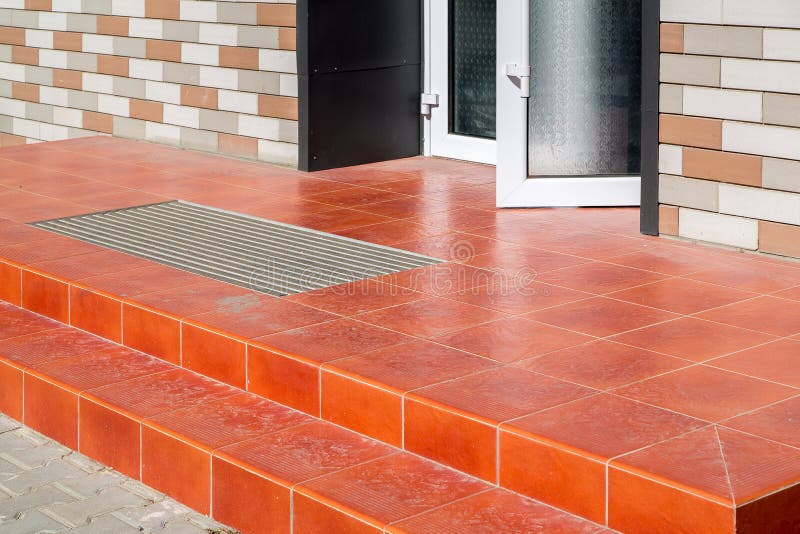 Threshold with a paved red tile and a foot mat at the open front door.