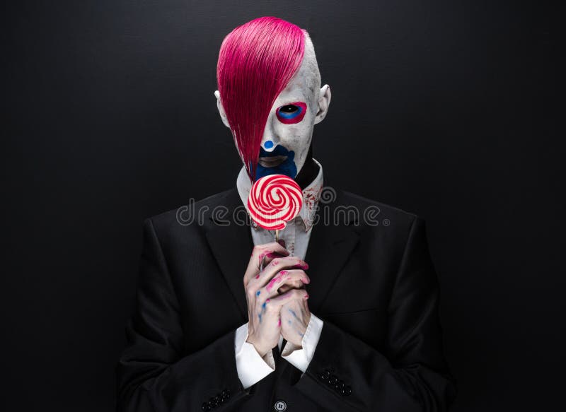 Thème de clown et de Halloween : Clown effrayant avec les cheveux roses dans une veste noire avec la sucrerie à disposition sur u photo libre de droits Thème de clown et de Halloween : Clown effrayant avec les cheveux roses dans une veste noire avec la sucrerie à disposition sur u photo libre de droits