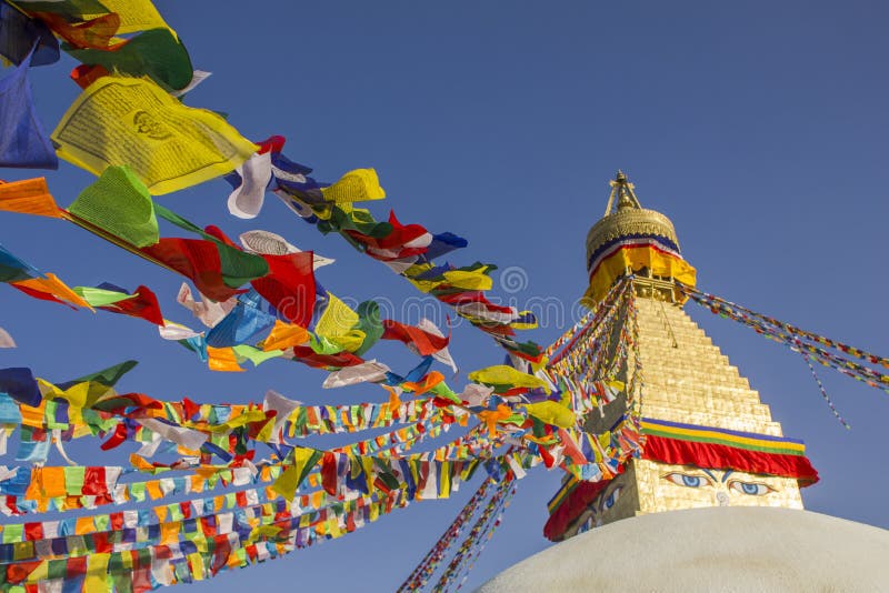 A Tibetan Buddhist Stupa Bodhnath with eyes and multicolored prayer flags against a clean blue sky at daytime