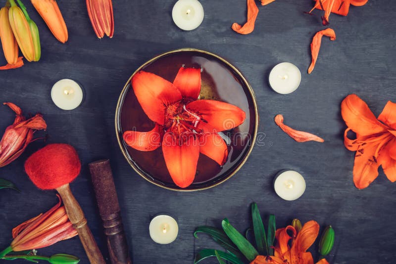 Tibetan singing bowl with floating in water lily inside. Special sticks, burning candles, lily flowers and petals on the black woo