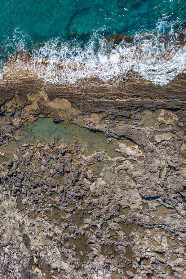 Tide pools during low tide on a rocky sea shore with dramatic texture, vertical top view