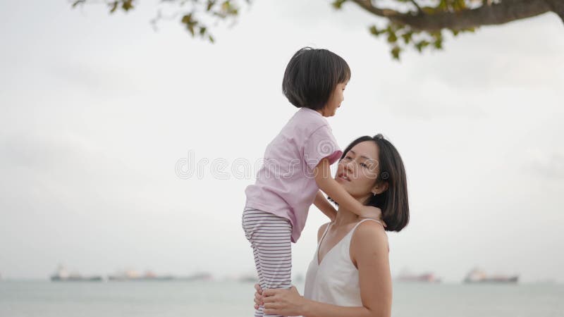 Tiempo de familia madre asiática levantando a hija al aire libre lado del mar almacen de metraje de vídeo