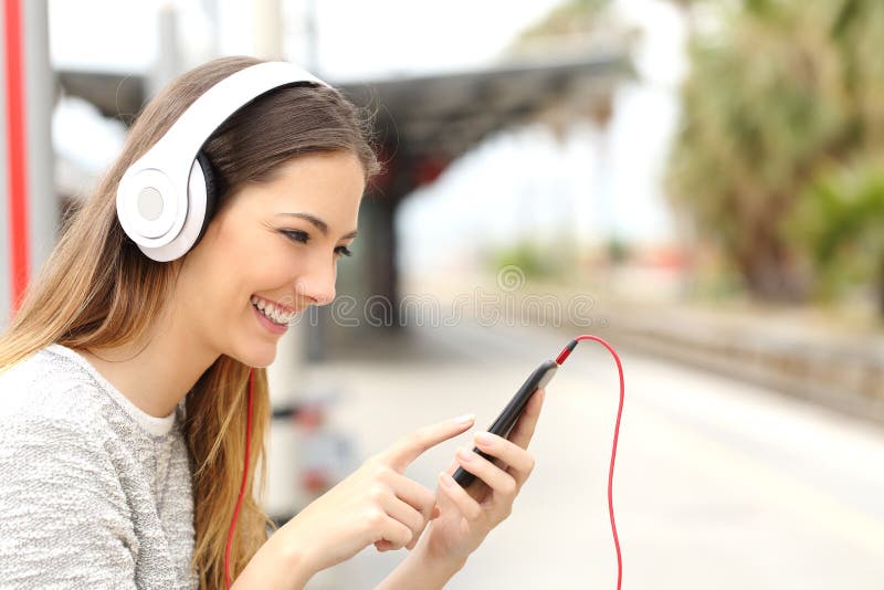 Tienermeisje die aan de muziek die met hoofdtelefoons luisteren een trein wachten