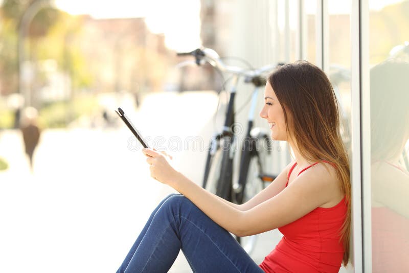 Tienermeisje die een tabletzitting in de straat gebruiken stock fotografie Tienermeisje die een tabletzitting in de straat gebruiken stock fotografie