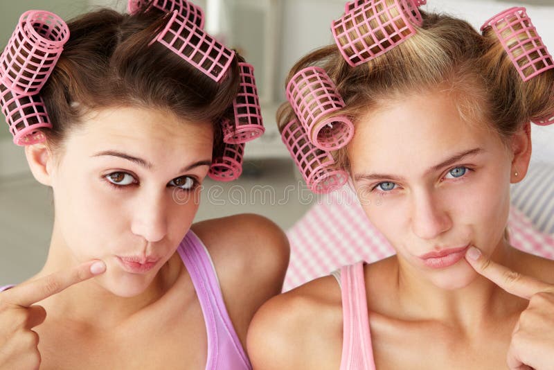 Teenage girls using curlers in their hair looking at camera. Teenage girls using curlers in their hair looking at camera