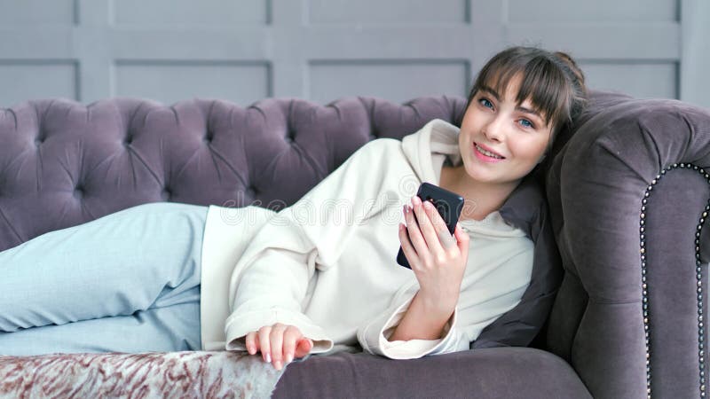 Tienervrouw die op laag in woonkamer het babbelen het schrijven bericht liggen die smartphone gebruiken