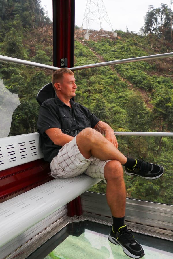 Land viewed through the glass floor of a Crystal Cabin. Man in cable car cabin with glass floor. Tourist rides on gondola lift. Genting Highland, Malaysia. Land viewed through the glass floor of a Crystal Cabin. Man in cable car cabin with glass floor. Tourist rides on gondola lift. Genting Highland, Malaysia.