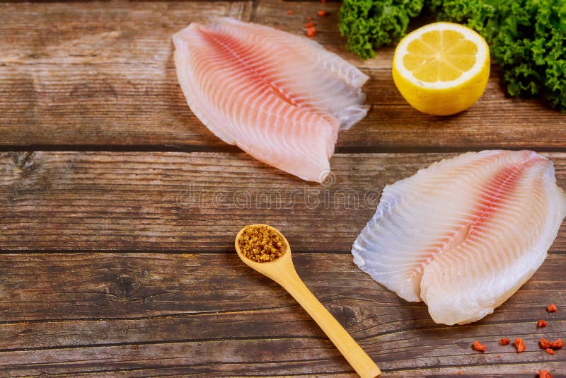 Tilapia de pescado orgánico sobre mesa con limón y condimento imagen de archivo