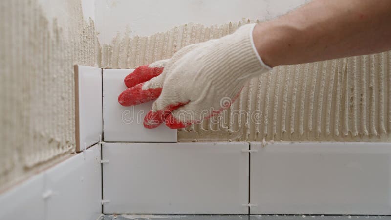 Tiler placing white ceramic tiles on wall with metal profile stock photography