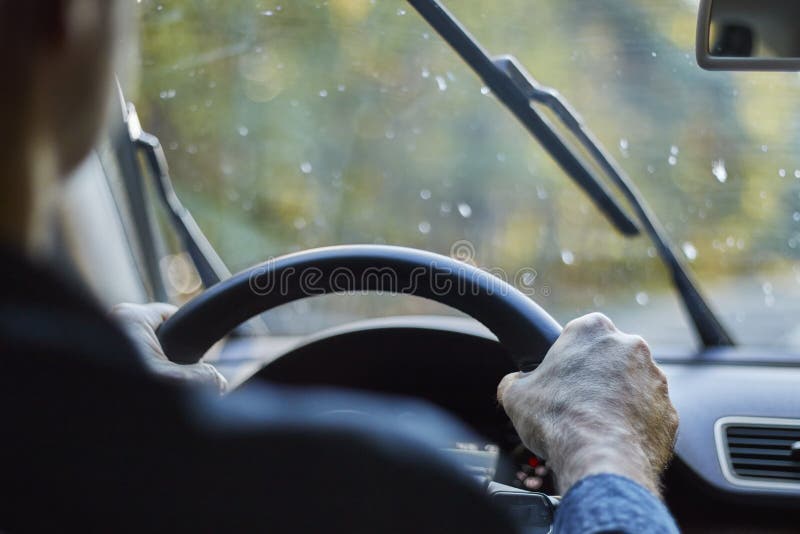 Tillbaka sikt av en man som kör en bil med rörande vindrutetorkare under regn