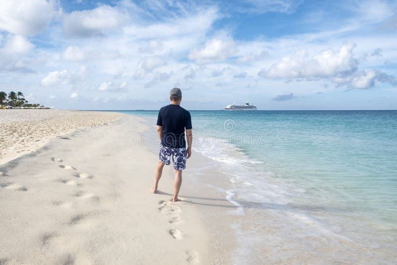 Tillbaka sikt av en man som står på en karibisk strand och ett kryssningskepp i avståndet royaltyfria bilder Tillbaka sikt av en man som står på en karibisk strand och ett kryssningskepp i avståndet royaltyfria bilder