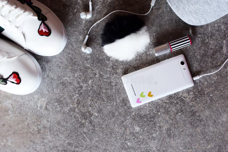 Tillbehör för flicka` s - vit smartphone, hörlurar, gymnastikskor och grått lock royaltyfri fotografi Tillbehör för flicka` s - vit smartphone, hörlurar, gymnastikskor och grått lock royaltyfri fotografi