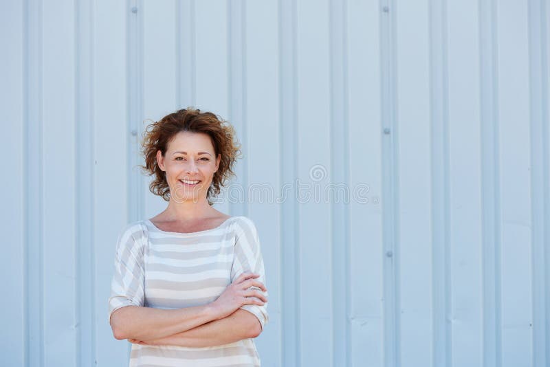 Tillfälligt lyckligt kvinnaanseende vid väggen med korsade armar