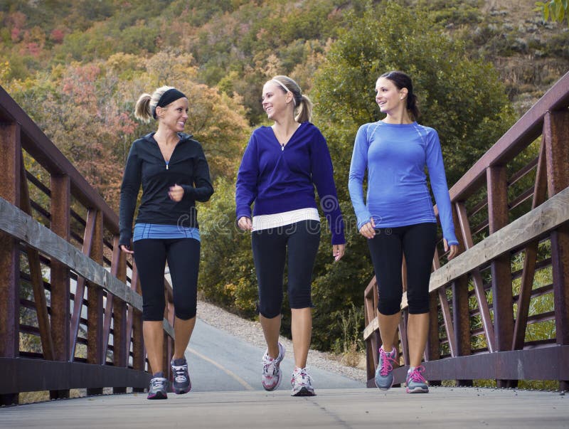 Three attractive young women talking a walk or jog together in the outdoors. Three attractive young women talking a walk or jog together in the outdoors