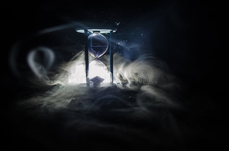 Time concept. Silhouette of Hourglass clock and smoke on dark background with blue cold back lighting, or symbols of time