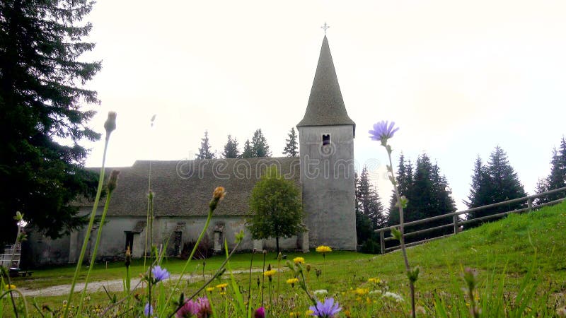 Time lapse, dramatic clouds above alpine church and meadow with flowers in front