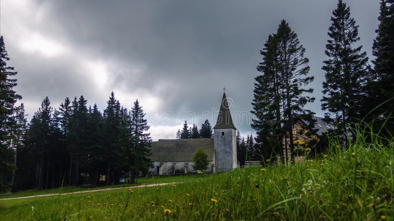 Time lapse, dramatic clouds above alpine village and church and meadow with flowers in front