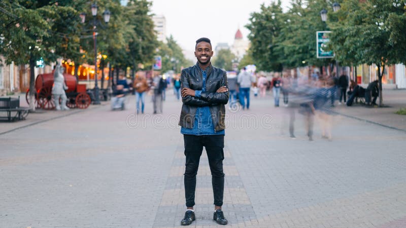 Time-lapse portrait of cheerful African American man standing in city center wearing stylish clothes looking at camera