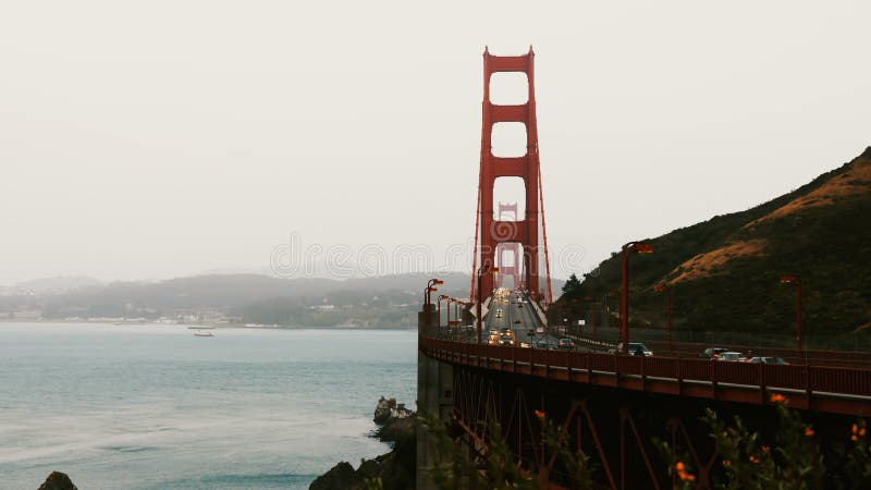 Time lapse shot of majestic sunset over iconic Golden Gate bridge, evening car traffic and flowers in San Francisco USA.