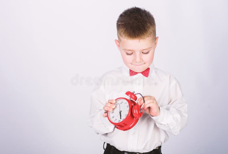 It is time. Morning routine. Schoolboy with alarm clock. Kid adorable boy white shirt red bow tie. Develop self