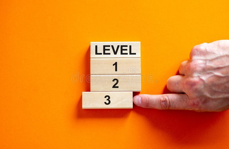 Time to level 3. Wooden blocks form the words `level, 1, 2, 3,` on orange background. Male hand. Beautiful background. Business