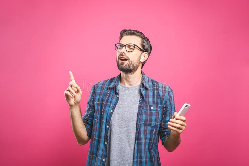 Time to relax. Handsome young man in headphones keeping eyes closed while dancing. Over pink background. Isolated