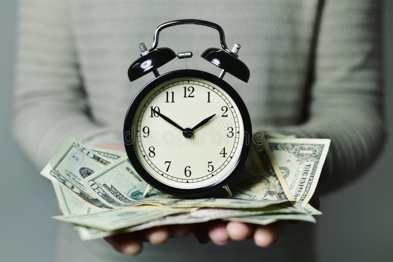 Closeup of a young caucasian man with an alarm clock and many US dollar banknotes in his hands, depicting the idea that time is money. Closeup of a young caucasian man with an alarm clock and many US dollar banknotes in his hands, depicting the idea that time is money