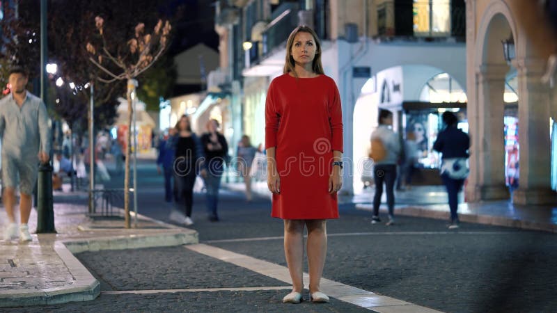 Timelapse of woman standing still on crowded evening street while a blur of fast moving people move around her