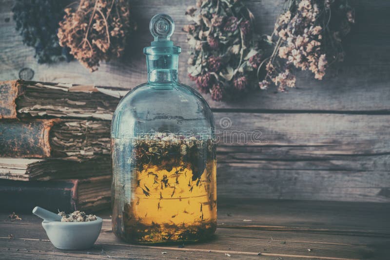 Tincture or potion bottle, old books, mortar and hanging bunches of dry healthy herbs. Herbal medicine.