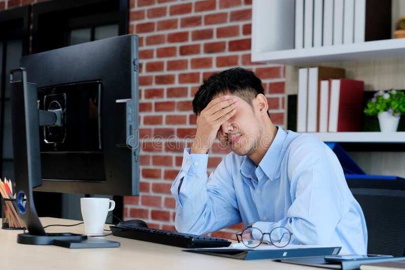 Tinere birouri asiatice se luptă cu un om de afaceri asiatic frustrat de calculator care se uită la calculator în timp ce lucrează stock image