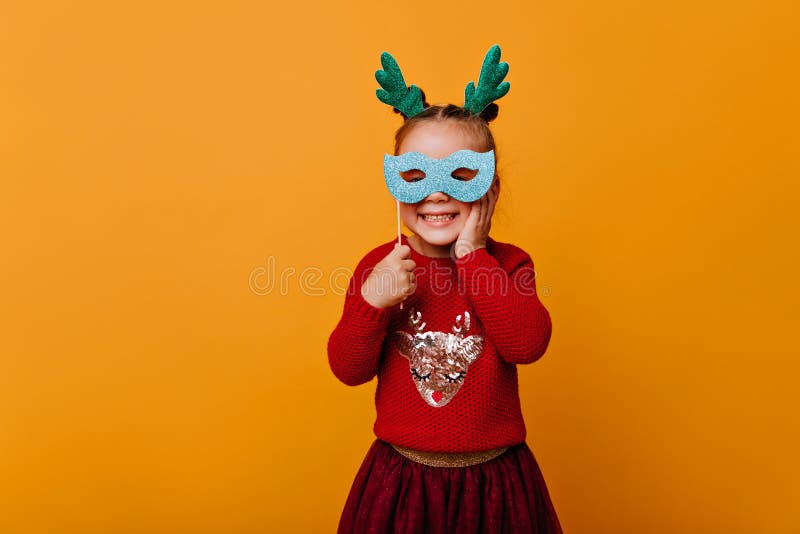 Tiny Girl In Red Bright Christmas Sweater With Pattern Of Shiny Deer Cute Looking At Camera And