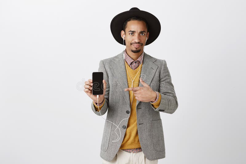 Tipo dispiaciuto che mostra cosa disgustosa in smartphone Ritratto di bello uomo alla moda deludente in black hat fotografie stock libere da diritti Tipo dispiaciuto che mostra cosa disgustosa in smartphone Ritratto di bello uomo alla moda deludente in black hat fotografie stock libere da diritti