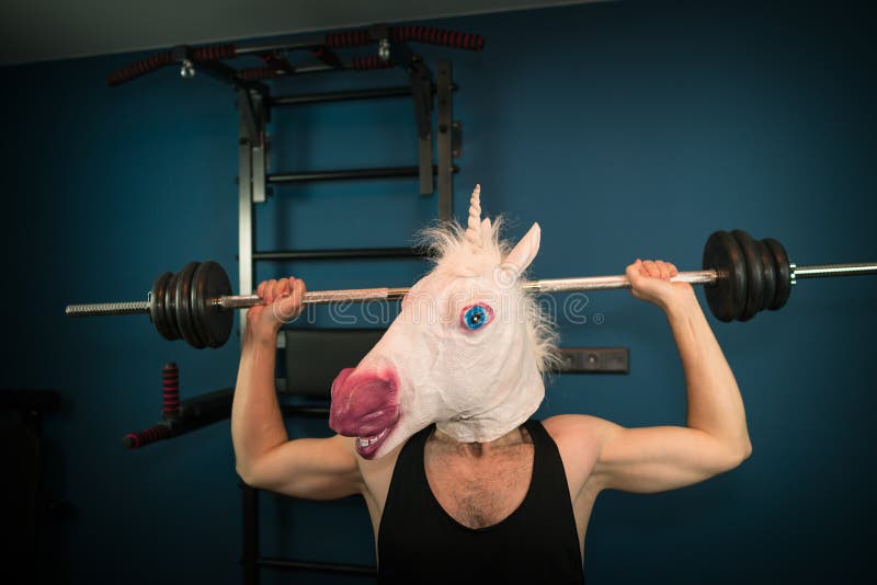 Funny guy in comical mask doing sport exercise. Unusual man pump up iron at home. Unicorn sportsman. Funny guy in comical mask doing sport exercise. Unusual man pump up iron at home. Unicorn sportsman.