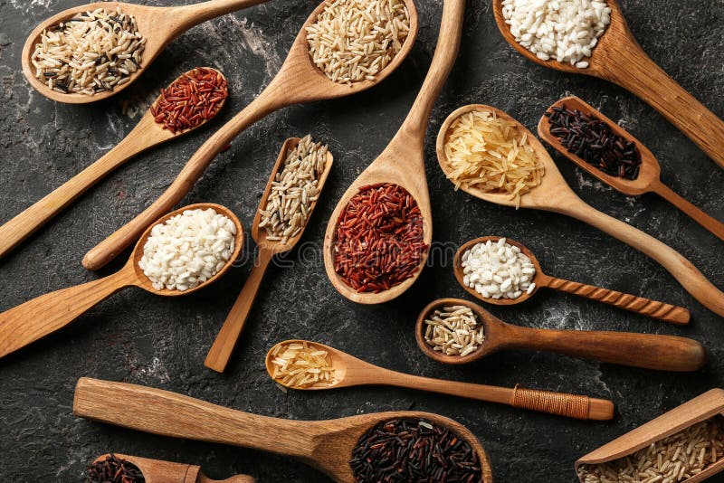 Tipos diferentes de arroz nas colheres no fundo cinzento