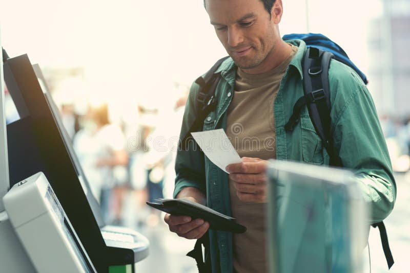 Tipul vesel așteaptă zborul. Călător avansat. Un om vesel cu rucsac stă în apropiere în chioșcul de selfservice și deține bilete. el este verificarea cardului său de îmbarcare. copiați spațiul în partea stângă