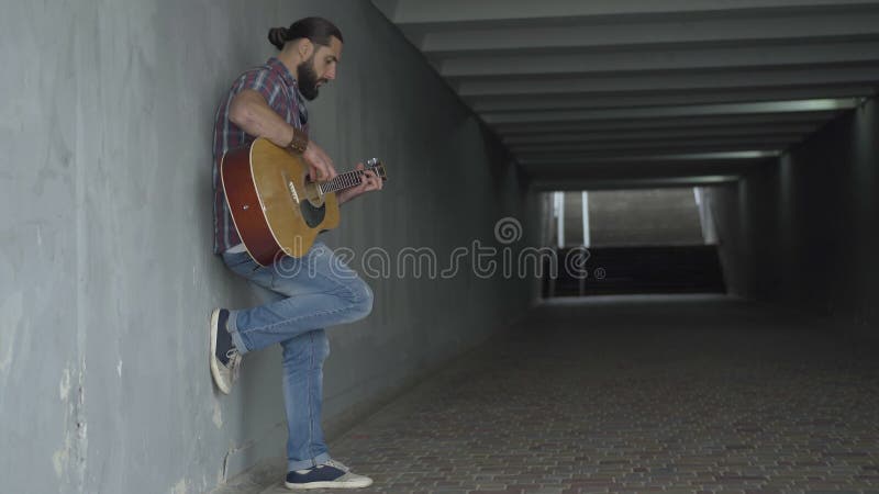 Tir de large vue de côté du guitariste caucasien rédigé jouant dans le passage souterrain Homme absorbé exécutant à urbain clips vidéos