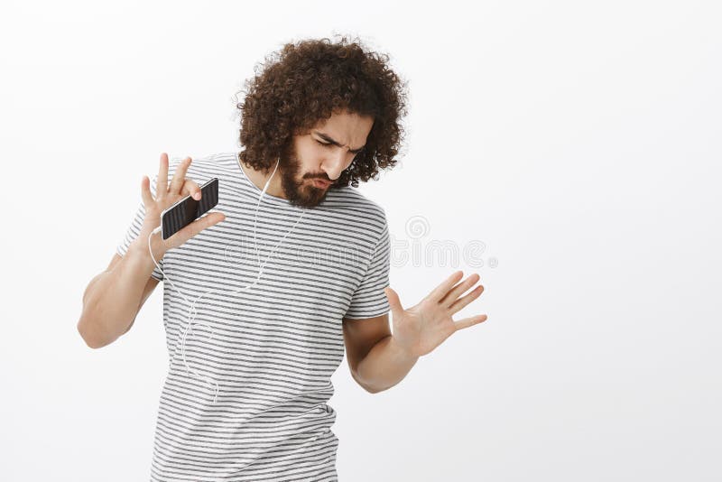 Tir de studio de modèle masculin beau insouciant enthousiasmé avec la barbe et la coiffure Afro, dansant et regardant vers le bas images libres de droits Tir de studio de modèle masculin beau insouciant enthousiasmé avec la barbe et la coiffure Afro, dansant et regardant vers le bas images libres de droits