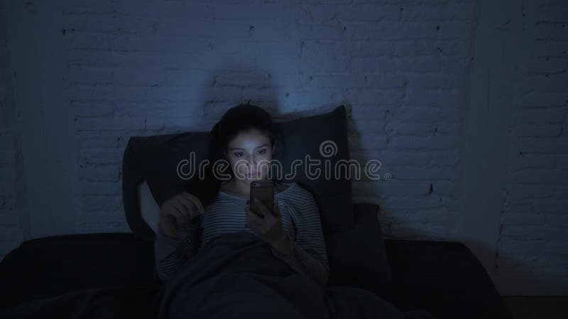 Tir frontal de jeune femme hispanique attirante sur son 30s se situant dans le lit de fin de nuit utilisant le regard de téléphon banque de vidéos