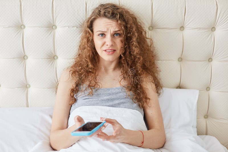 Tir horizontal de la jeune femelle avec des émotions incompréhensibles, fille avec les cheveux bouclés habillés dans la chemise d photographie stock Tir horizontal de la jeune femelle avec des émotions incompréhensibles, fille avec les cheveux bouclés habillés dans la chemise d photographie stock
