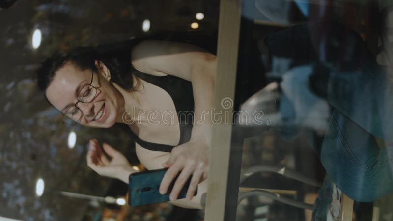 Tir vertical d'une femme tenant le téléphone cellulaire dans un caffe. parler à un ami sur un téléphone portable pendant une pause clips vidéos