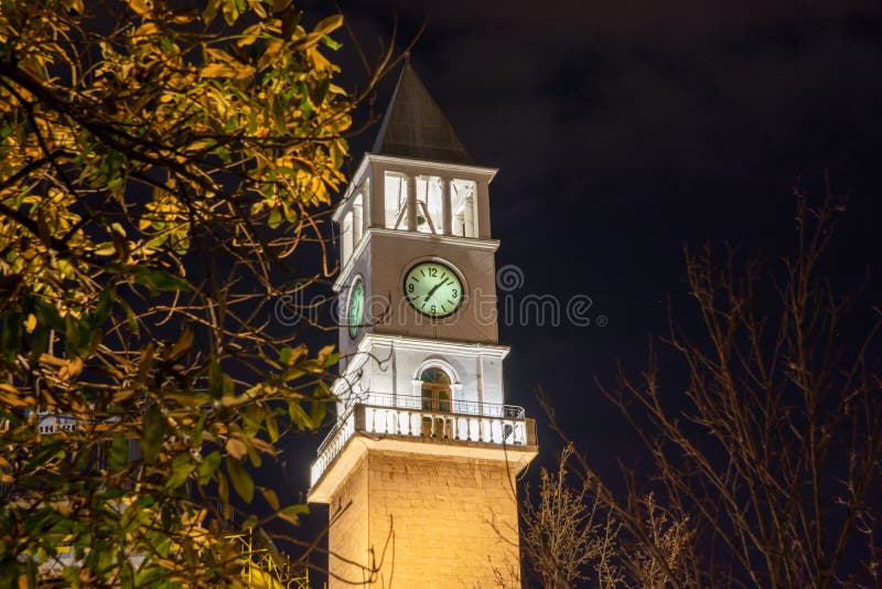 Tirana, Albania - March 16 2021: Clock Tower close-up behind trees night shot