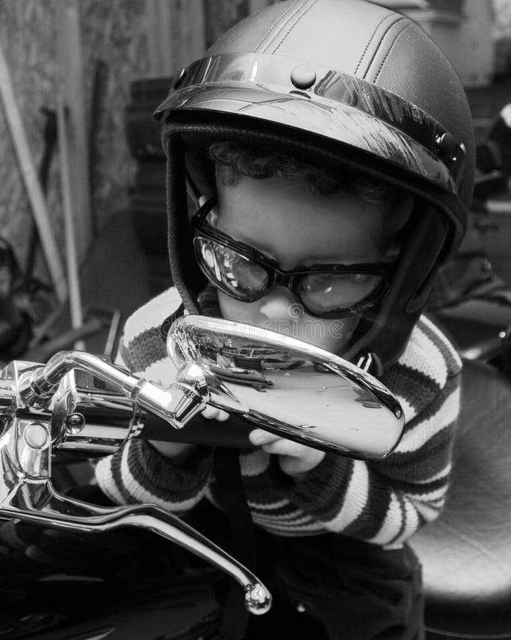 Little boy on a motorcycle in a garage with dad's helmet and glasses, in black and white. Little boy on a motorcycle in a garage with dad's helmet and glasses, in black and white.