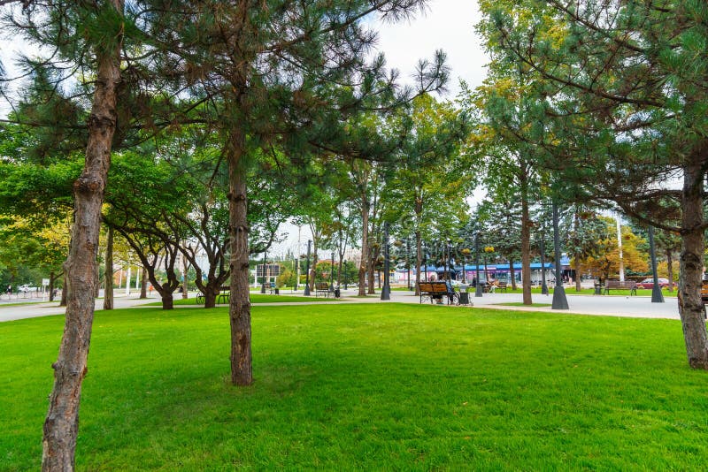 Tiraspol, Transnistria, Moldova - September 6, 2022: city park, green lawns and trees, random people walking along the paths, urban architecture. Tiraspol, Transnistria, Moldova - September 6, 2022: city park, green lawns and trees, random people walking along the paths, urban architecture